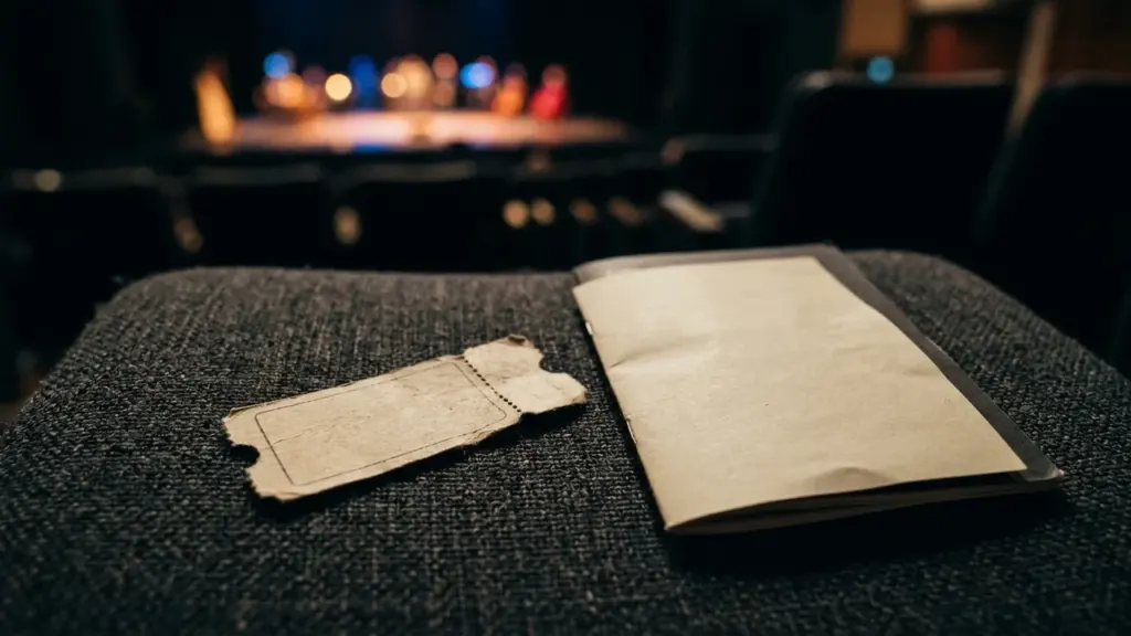 Un vieux ticket de spectacle et un carnet posés sur un siège de théâtre sombre.