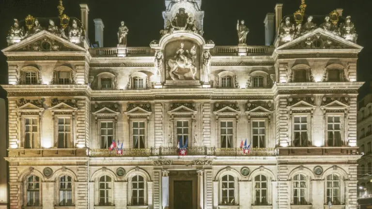 L'Hôtel de Ville de Lyon illuminé sous un ciel nocturne avec ses statues.