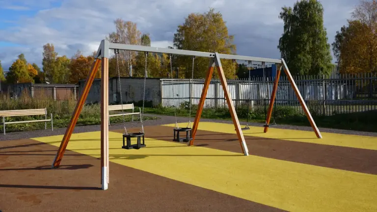 Aire de jeux publique avec balançoires modernes dans un parc urbain verdoyant.
