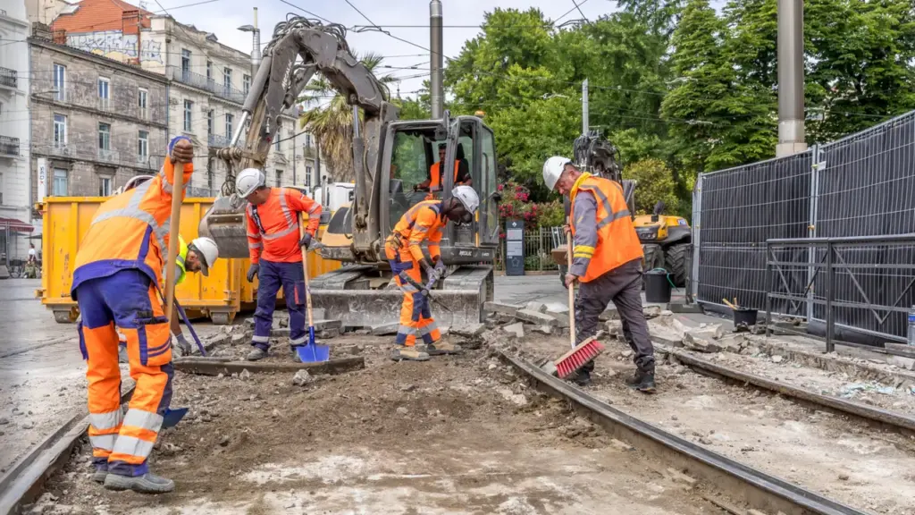 Ouvriers en vêtements de sécurité travaillant sur des rails de tramway en milieu urbain.