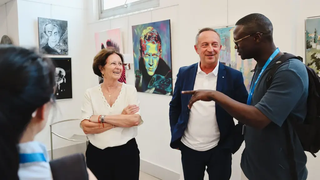 Trois personnes discutent joyeusement dans une galerie d'art devant des peintures colorées exposées.