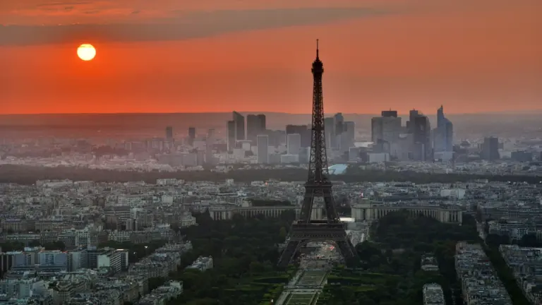 Vue aérienne panoramique de Paris sous un soleil couchant intense et orangé.
