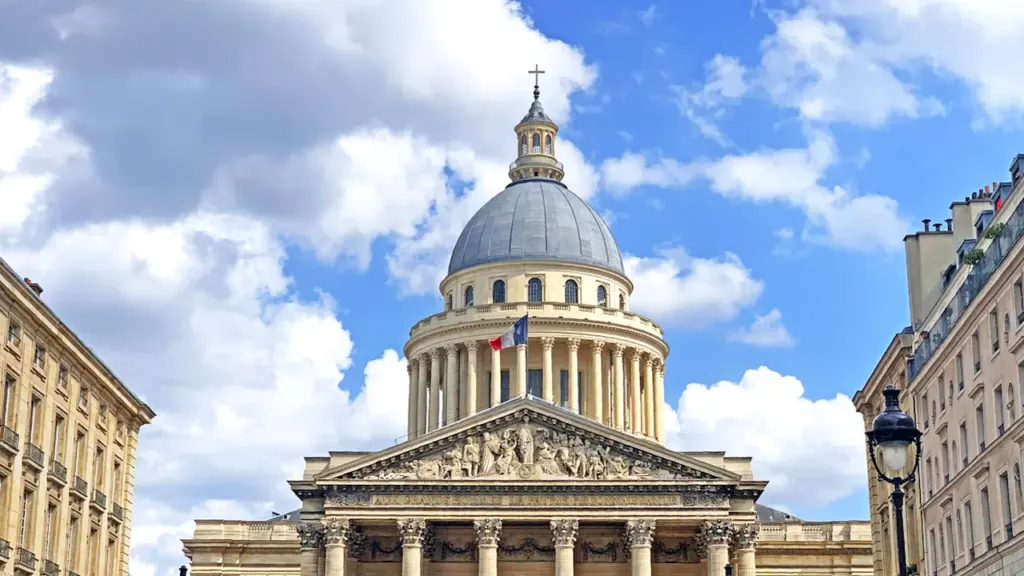 Le Panthéon à Paris sous un ciel bleu avec le drapeau français flottant.