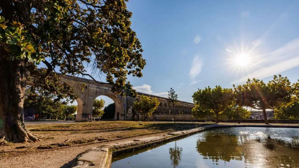 Vaste aqueduc romain en pierre surplombant un parc ensoleillé avec un bassin d'eau calme.
