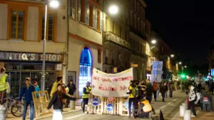 Manifestation nocturne dans une rue de Toulouse avec des banderoles et des passants.