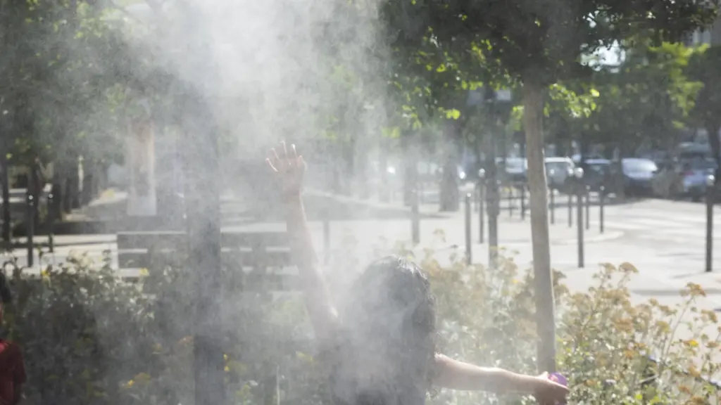 Une personne de dos lève les bras dans un nuage de brume rafraîchissante urbaine.