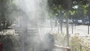 Une personne de dos lève les bras dans un nuage de brume rafraîchissante urbaine.