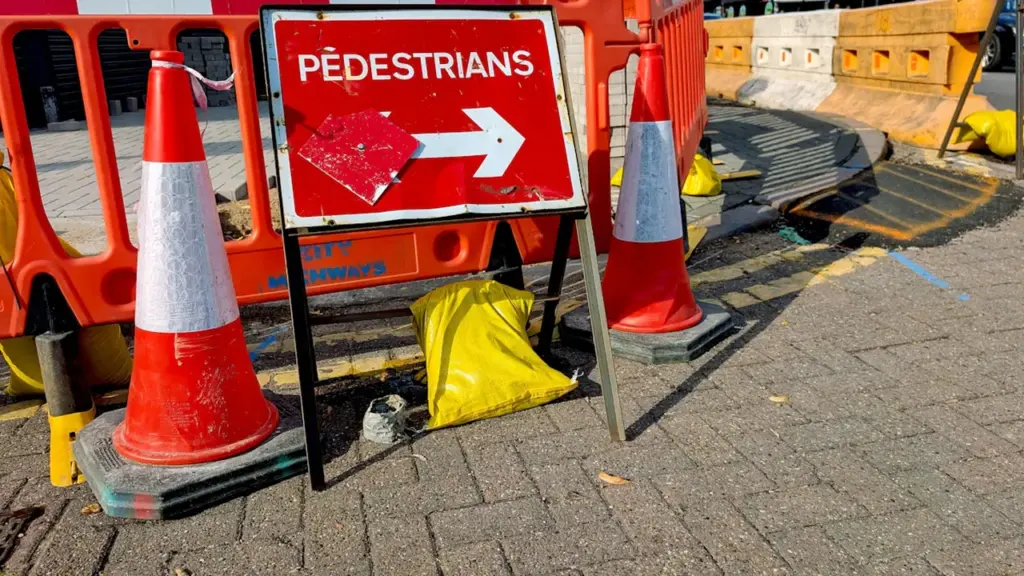 Panneau de signalisation et cônes de chantier sur un trottoir urbain ensoleillé.