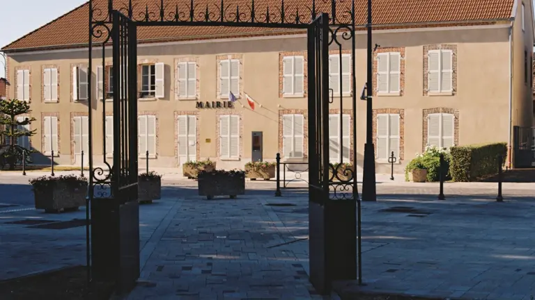 Façade de la mairie d'Épinay-sous-Sénart vue à travers une grille en fer forgé.