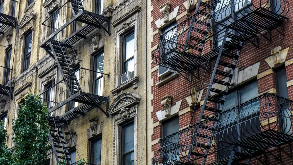 Façade d'immeubles en briques avec escaliers de secours extérieurs et climatiseurs.