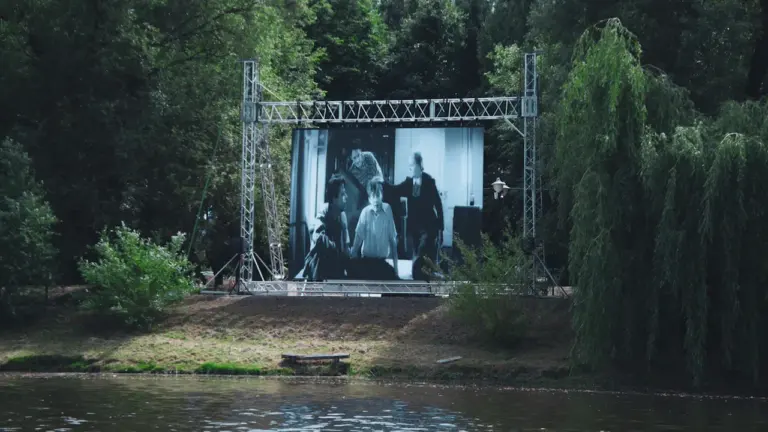 Un grand écran de cinéma installé en plein air au bord d'un parc arboré.