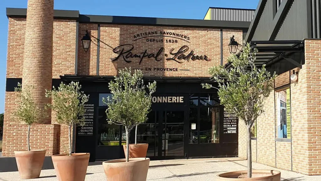 Façade en briques de la savonnerie Rampal Latour avec des oliviers en pots devant.