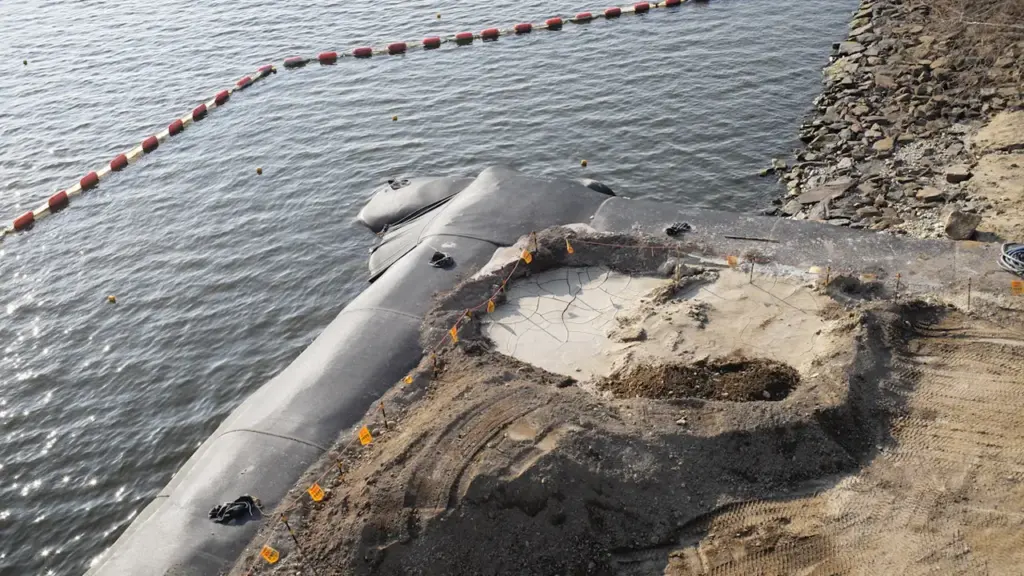 Chantier de protection contre les inondations avec barrières et terrassements près d'une rive.