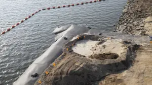 Chantier de protection contre les inondations avec barrières et terrassements près d'une rive.