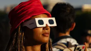 Une femme avec un turban rouge porte des lunettes de protection pour observer l'éclipse solaire.