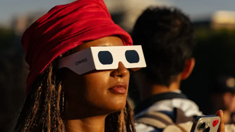Une femme avec un turban rouge porte des lunettes de protection pour observer l'éclipse solaire.