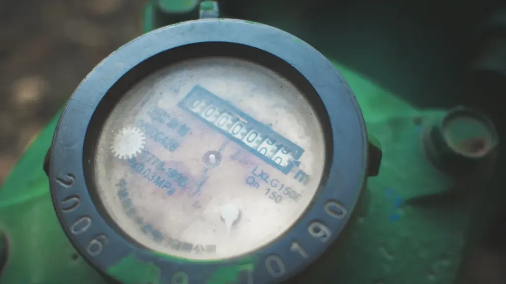 Compteur d'eau noir circulaire installé sur une conduite murale résidentielle.