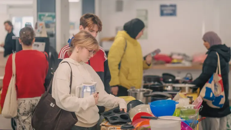 Une jeune femme regarde des ustensiles de cuisine lors d'une vente solidaire en intérieur.