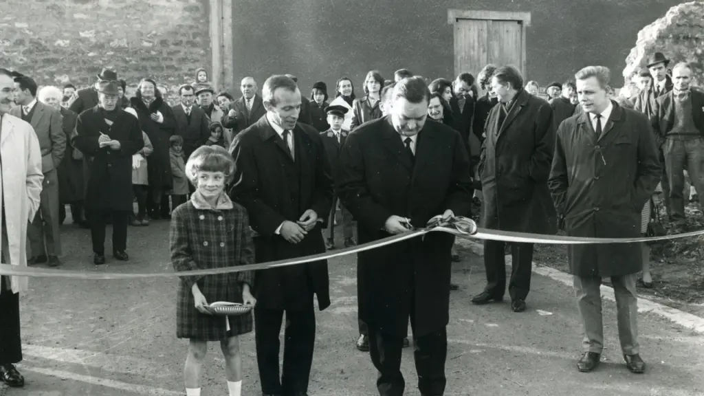 Un homme en costume coupe un ruban entouré d'une foule et d'une jeune fille.