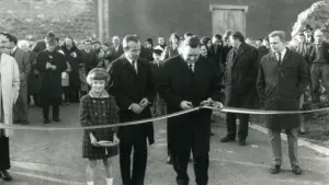 Un homme en costume coupe un ruban entouré d'une foule et d'une jeune fille.