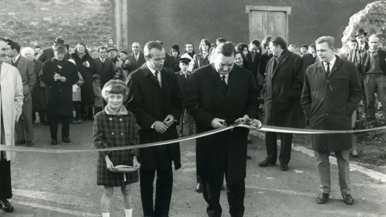 Un homme en costume coupe un ruban entouré d'une foule et d'une jeune fille.