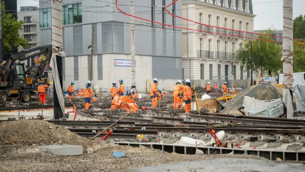 Des ouvriers en vêtements orange travaillent sur un chantier de construction de lignes de tramway.