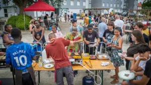 Des personnes préparent et servent de la nourriture lors d'un barbecue communautaire en extérieur.