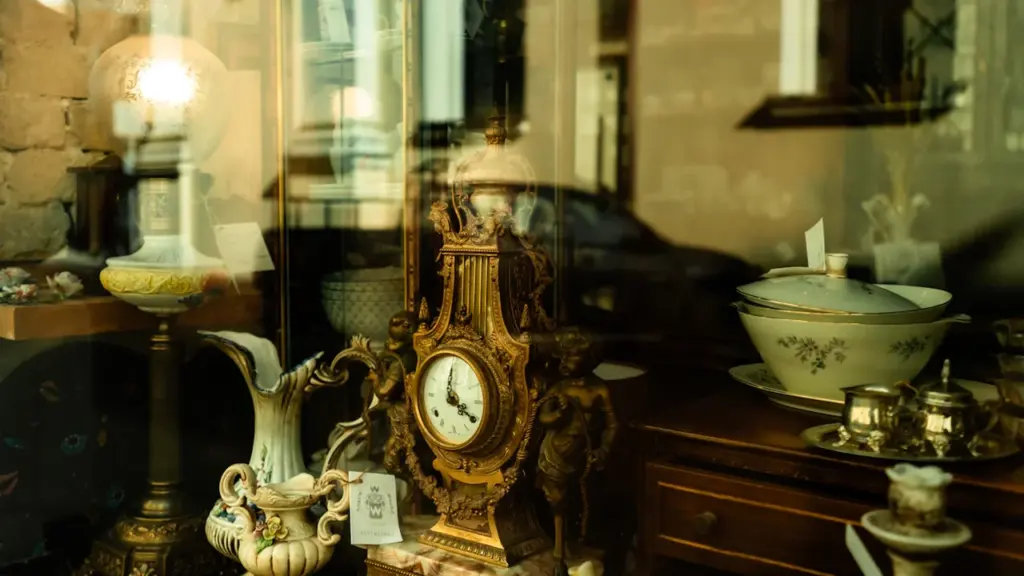 Objets anciens, horloges et vaisselle présentés derrière une vitrine de boutique spécialisée.