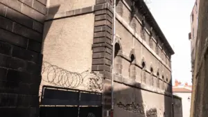Une ruelle étroite bordée par un bâtiment ancien aux murs protégés par des barbelés.