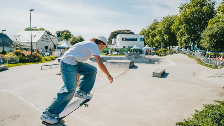 Un jeune skateur en t-shirt blanc effectue une figure sur une rampe en béton.