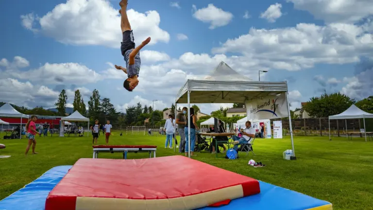 Un jeune garçon réalise un salto arrière au-dessus d'un tapis de gymnastique dans un parc.