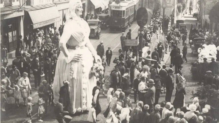 Une foule observe une marionnette géante lors d'une parade dans une rue historique animée.