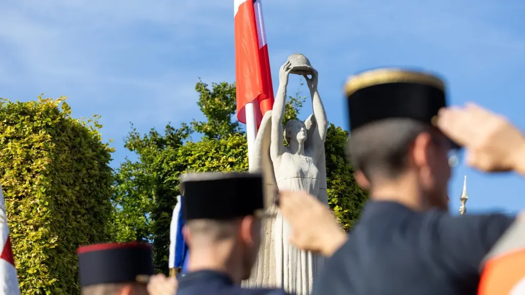 Militaires en uniforme saluant devant une statue de pierre représentant une femme soulevant un casque.