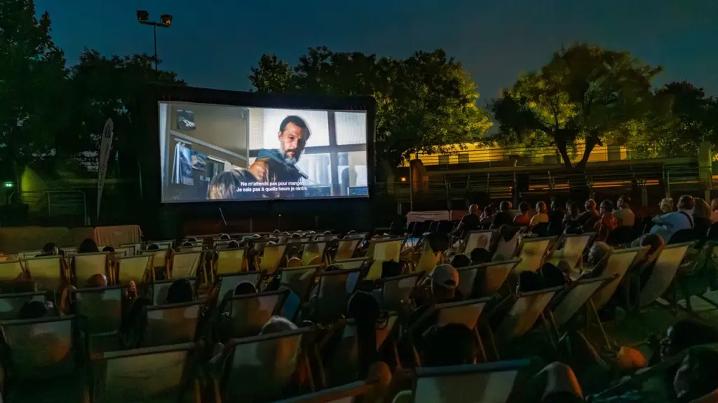 Public en plein air assis sur des chaises longues regardant un film sur écran géant.