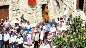 Un groupe de personnes en costumes traditionnels devant une statue en bois sur une place.