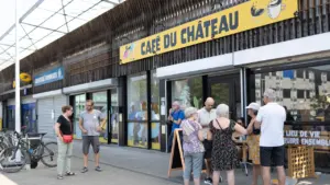 Un groupe de personnes discute devant la devanture jaune du Café du Château extérieur.