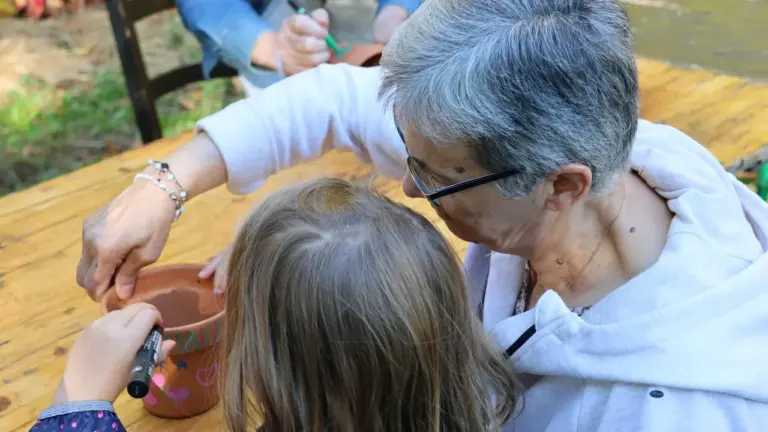 Une femme âgée et une jeune enfant peignent ensemble un pot en terre cuite.